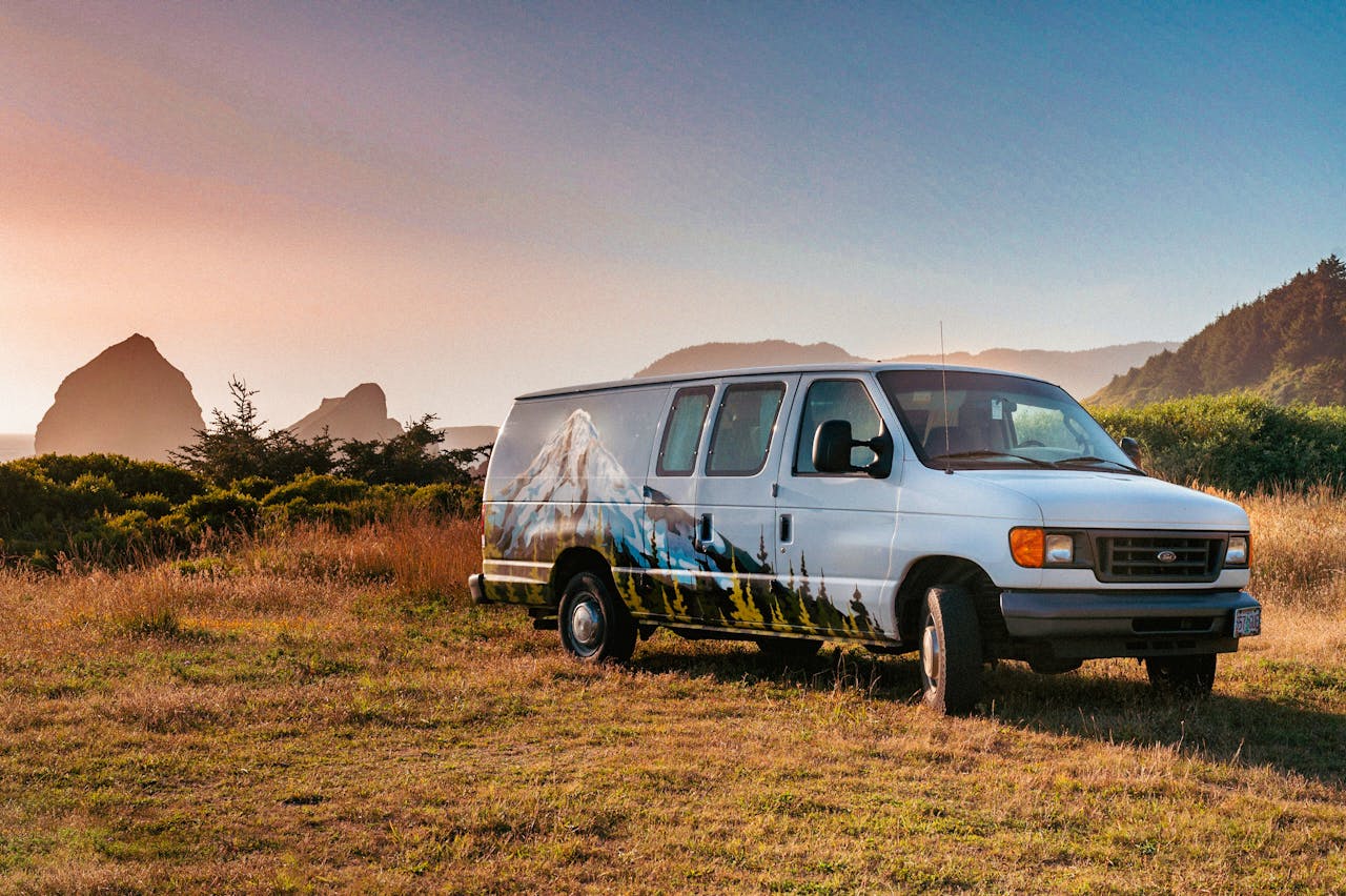 Van with mountain mural parked in a scenic setting during sunset, ideal for nature and travel themes.