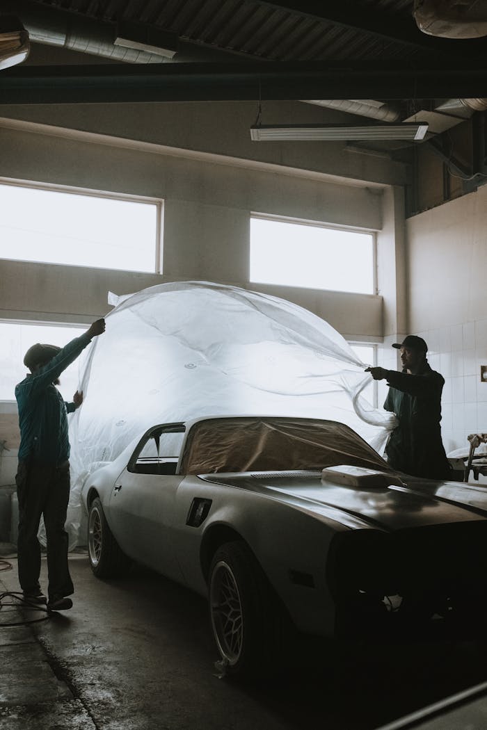 about-me-01 Mechanics working on classic car restoration inside a well-lit garage space.